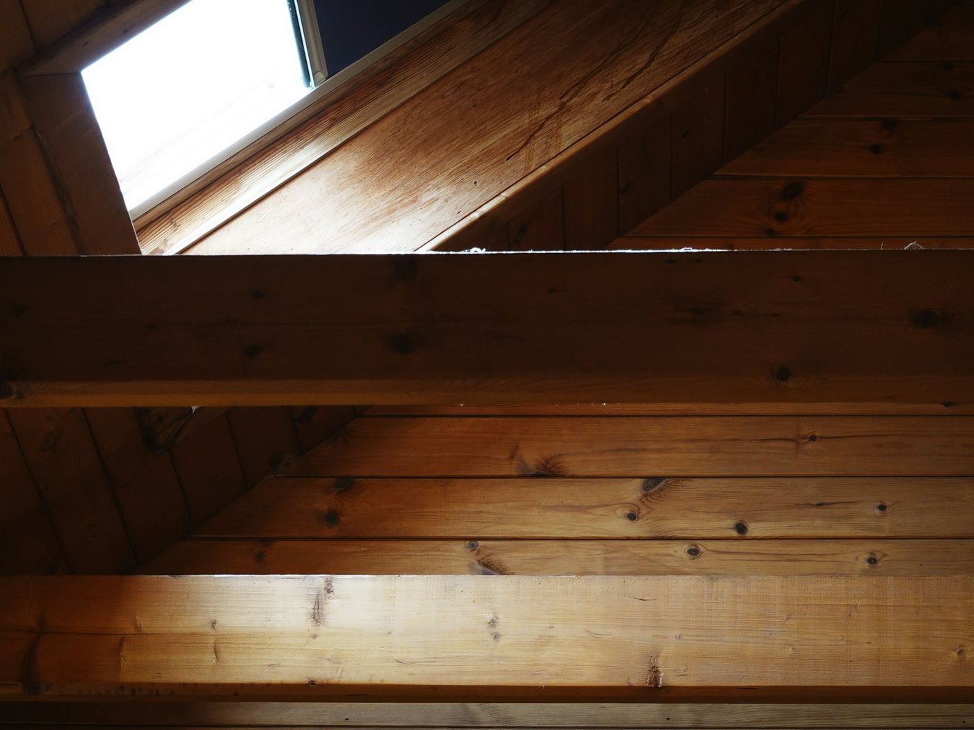 Dachgeschoss mit Holzbalken und Holzverkleidung, Licht fällt durch ein Dachfenster